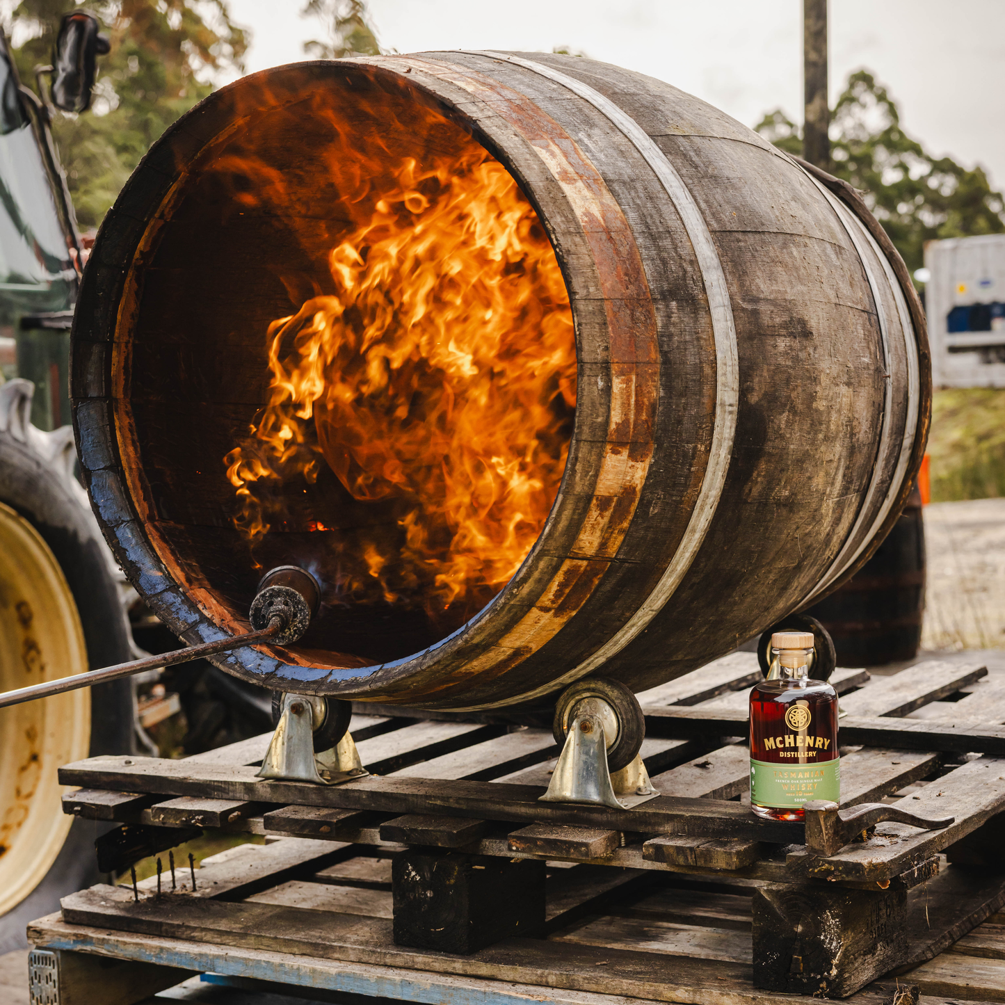 Flaming whiskey barrel with a bottle of McHenry Whiskey on a pallet.