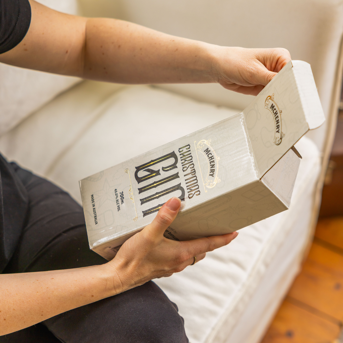 Person holding a McHenry Christmas gin box on a white couch.
