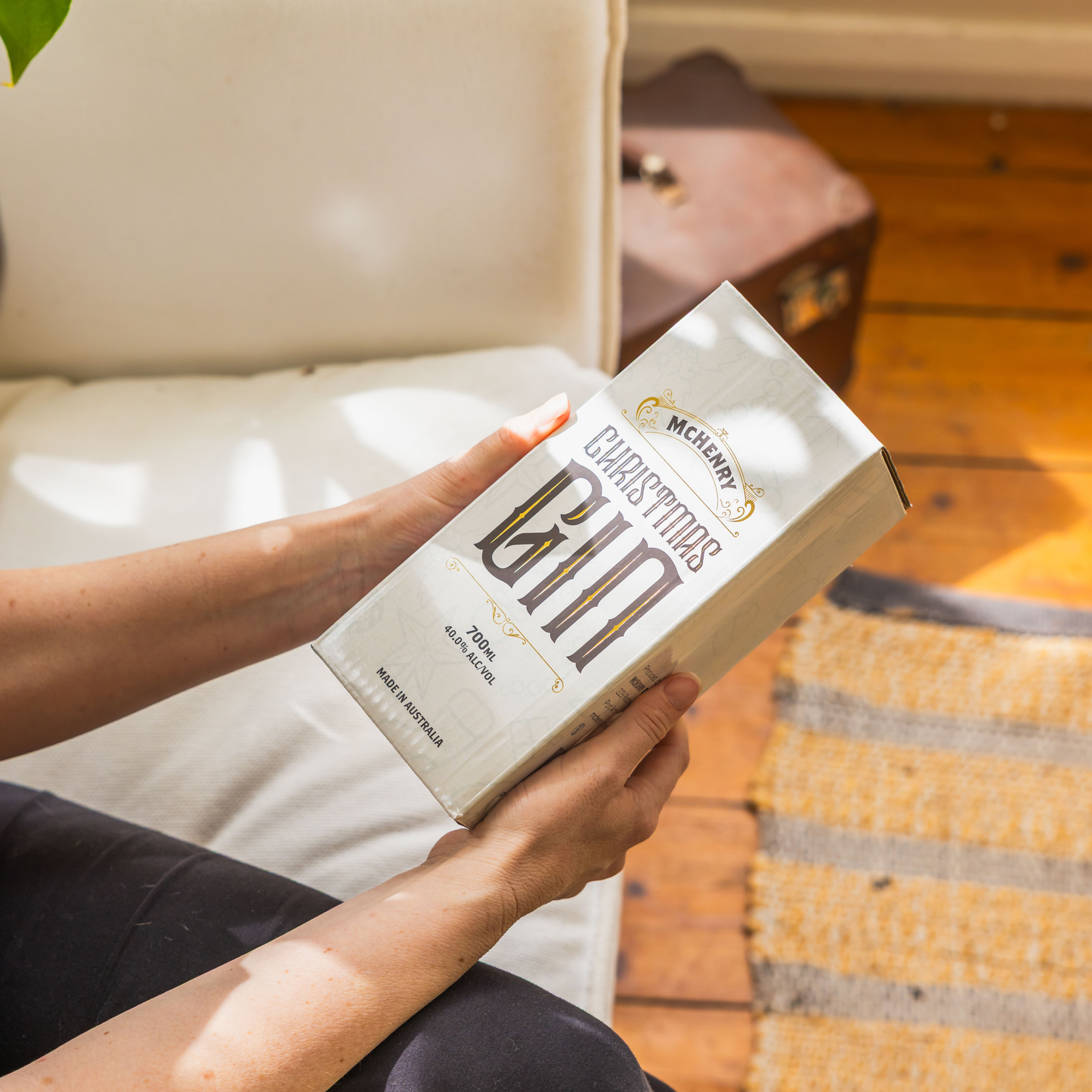 Person holding a box of McHenry Christmas Gin Gift box on a couch.