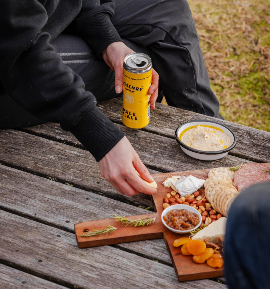Person sitting at a wooden table outdoors with food and a can.